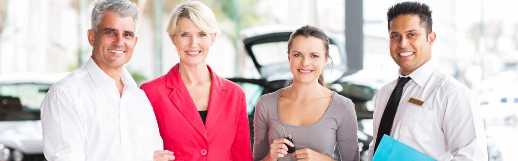 A professional vehicle sales team, all smiling in the well-lit showroom and prepared to help new customers