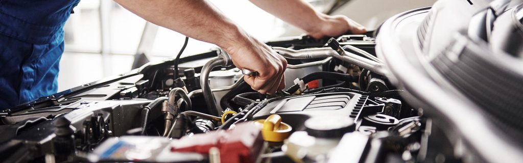 A certified professional mechanic is making adjustments on a GMC SUV engine