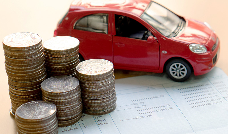 A miniature red SUV sits with one tire and 5 stacks of coins on a New Car Financing plan sheet.